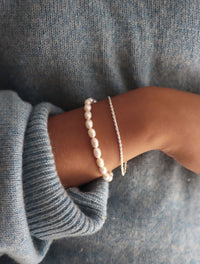 Tjej som bär ett smalt pärlarmband kombinerat med silverarmband. 