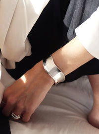 tjej som bär ett brett stelt silverarmband med vågig form.