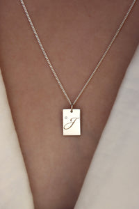 Tjej som bär ett halsband med bokstavsberlock i silver med liten diamant