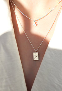 Tjej som bär bokstavshalsband. En diamantbokstav i kort kedja och en berlock med rektangulär bricka och graverad bokstav + diamant.