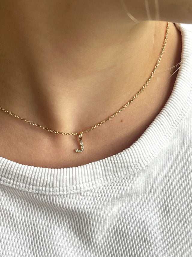 Tjej som bär ett kort guldhalsband med diamantbokstav. 