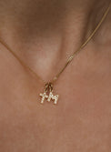 Kvinna som bär ett halsband med ett diamantkors i guld och en bokstavsberlock i guld med diamanter. 