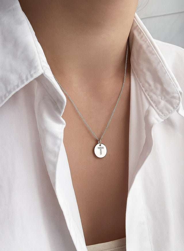 tjej som bär ett halsband med rund berlock som har diamantbokstav T. 