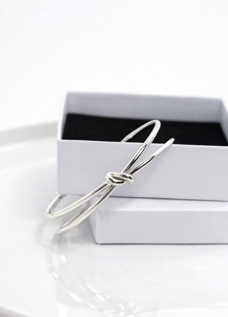 Stelt silverarmband med knut placerat på en vit smyckesask. 