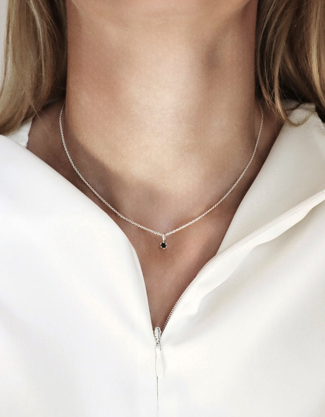 kvinna bär ett halsband med en liten svart diamant. 