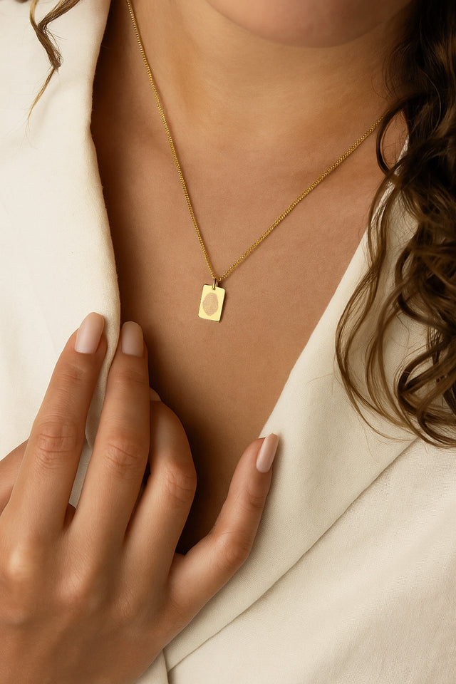 Kvinna som bär ett halsband i 18k. guld med berlock som har graverat fingeravtryck. 