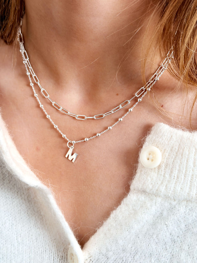 Tjej som bär ett kort kedjehalsband med Paperclip kedja kombinerat med ett bokstavshalsband. 