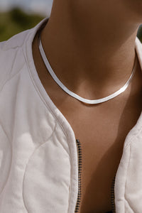 kvinna som bär en herringbone kedja, 5 mm bred, i kort choker längd. Silvervit kedja med fin lyster mot solbrun hud. 