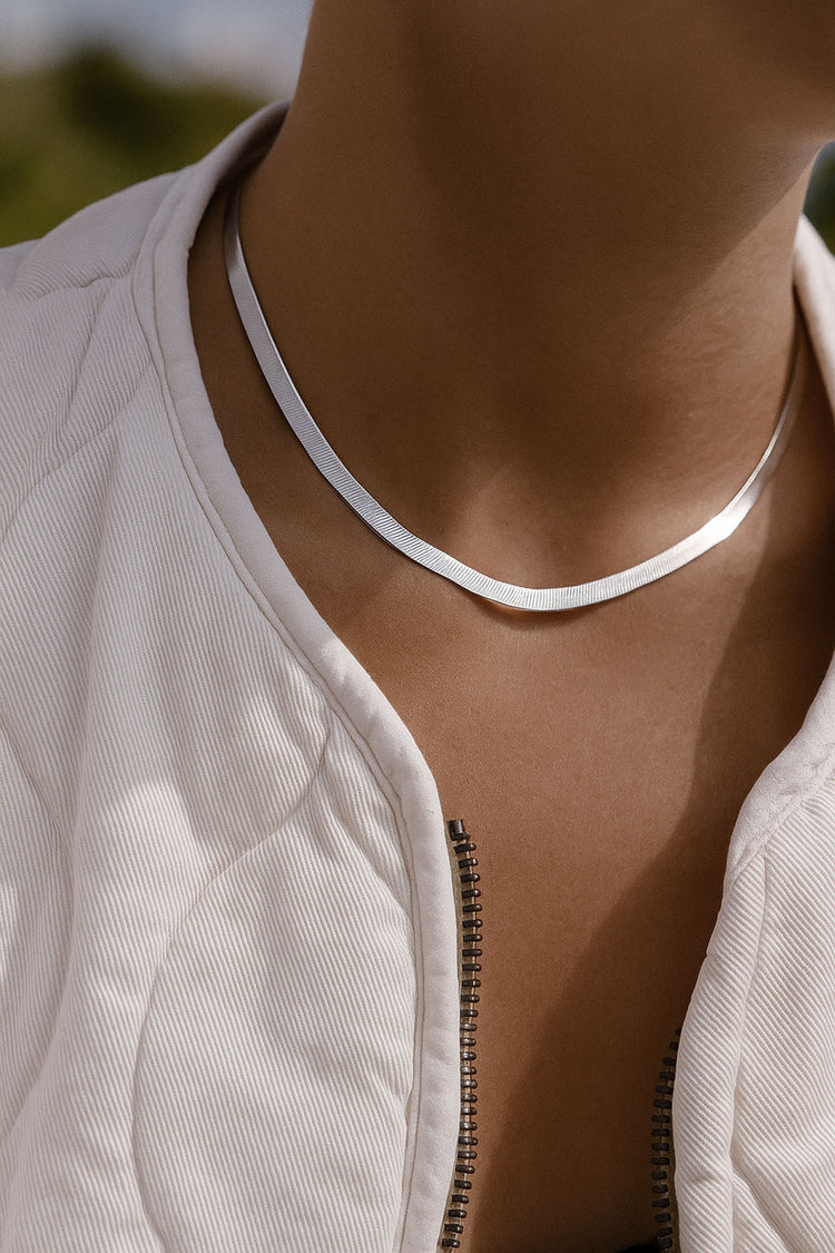 kvinna som bär en herringbone kedja, 5 mm bred, i kort choker längd. Silvervit kedja med fin lyster mot solbrun hud. 