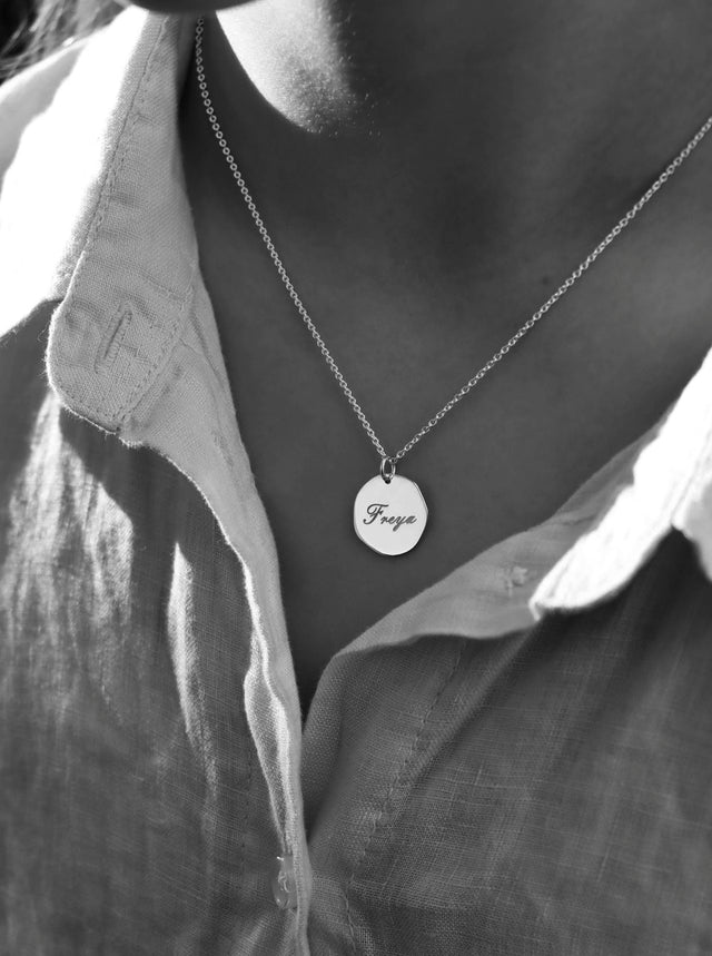 tjej som bär ett halsband med silverberlock som har graverat namn i skrivstil. 