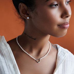 Tjej som bär ett pärlhalsband, kort choker halsband med vita små pärlor och hjärta i 925 silver. 
