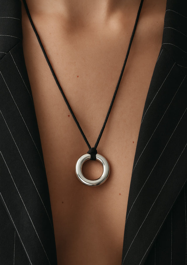 Halsband med silverring i läderband på modell som har randig kavaj uppknäppt. 