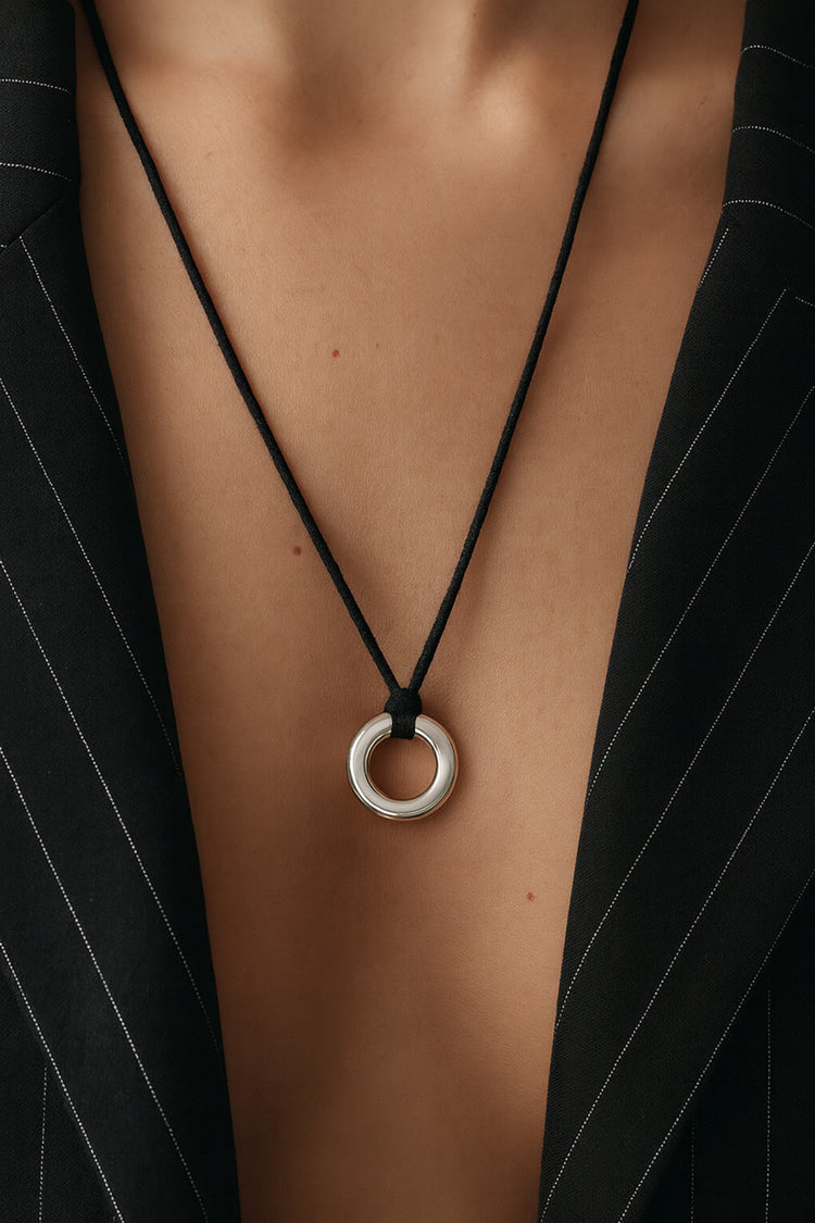 Kvinna som bär ett halsband med ring i silver i svart läderband. Hon bär en svart kavaj med djup urringning. 