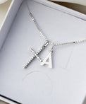 Halsband med silverkors och bokstavsberlock placerat i en vit smyckesask från Mila Silver