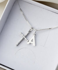 Halsband med silverkors och bokstavsberlock placerat i en vit smyckesask från Mila Silver