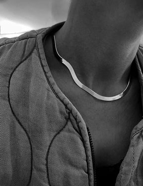 Tjej som bär en platt ormkedja i silver med fin lyster. kedjan är 5 mm bred och kort runt halsen. 