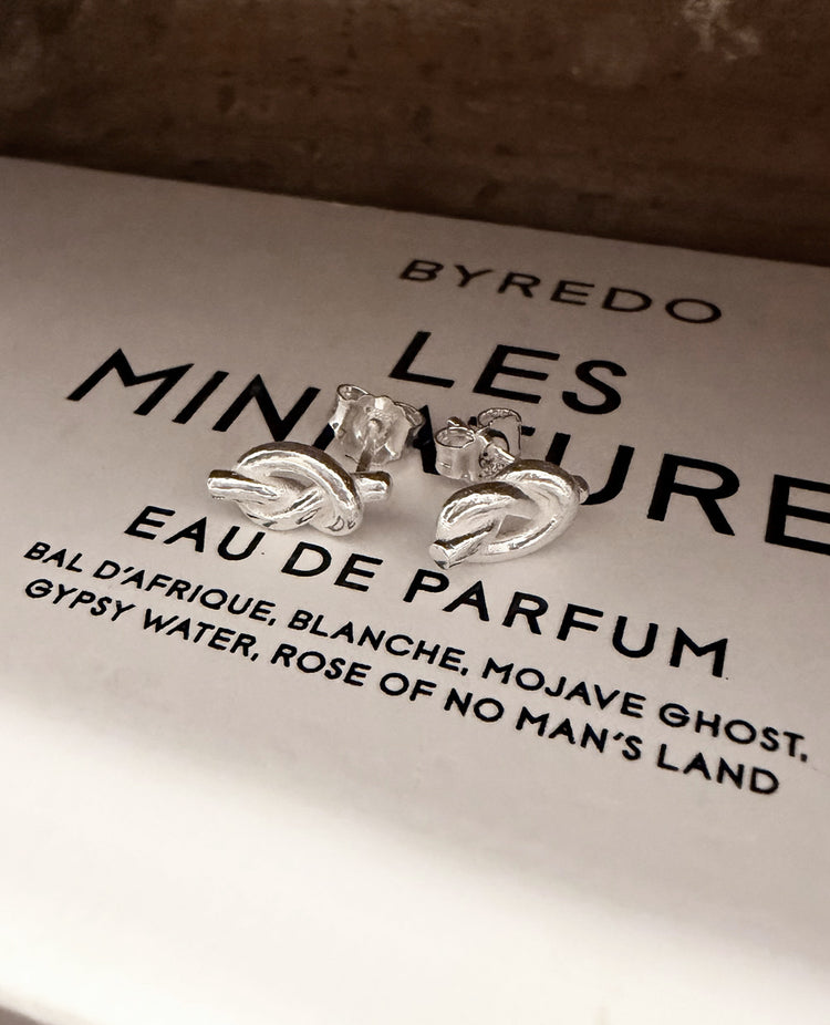 Örhängen med silverknutar ligger på vit ask från parfume märket Byredo. 