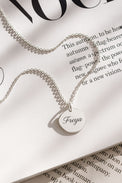 halsband med graverat namn på en berlock i silver, placerad på ett magasin. 