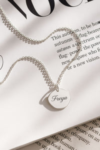 halsband med graverat namn på en berlock i silver, placerad på ett magasin. 