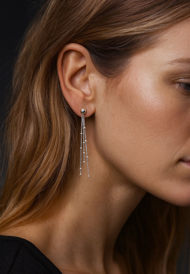 Tjej som bär långa hängande örhängen med kedjor och kulor i äkta silver. 