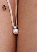 Berlock med pärla och diamant i läderband, placerad mellan två ben, ett litet bi kryper på benet. 