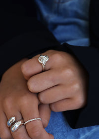 Tjej som bär en silverring med knut på pekfingret, kombinerat med flera andra silverringar på andra handen. 