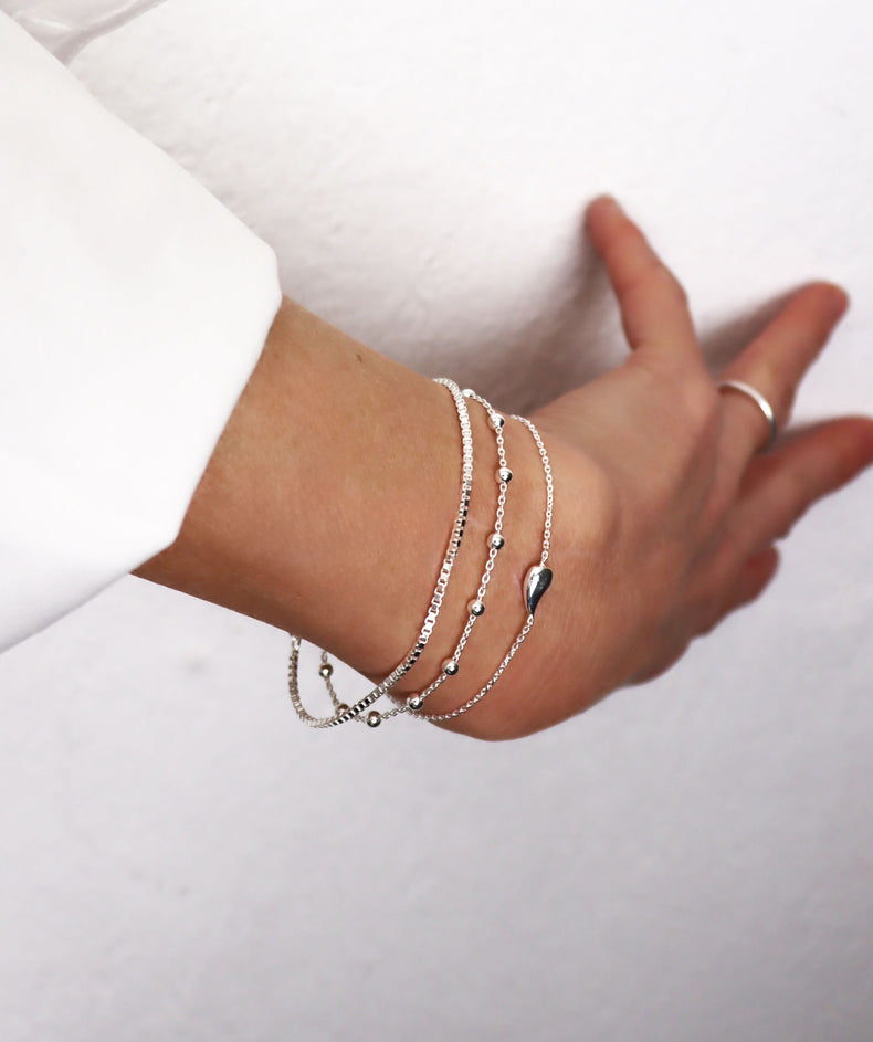 Tjej som bär flera tunna silverarmband i kombination.