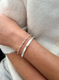 Tjej som bär två silverarmband ett med kulor och ett stelt silverarmband. 