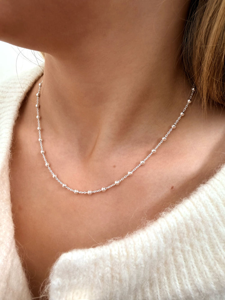 Tjej som bär ett kort, fint silverhalsband med tunn kedja och små silverkulor. 