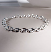 Närbild på ett brett kedjehalsband med ovala tjocka länkar. 