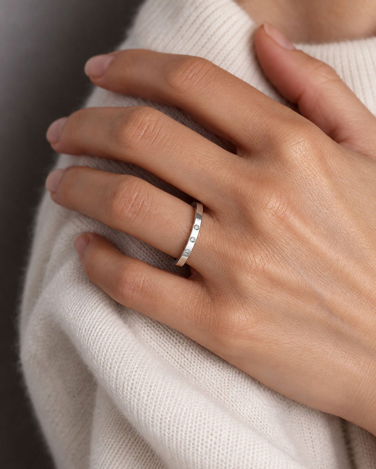 Tjej som bär en silverring med tre diamanter på rad som sitter nedsänkta i ringen