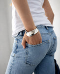Tjej som bär ett brett, stelt silverarmband till jeans och vit t-shirt.