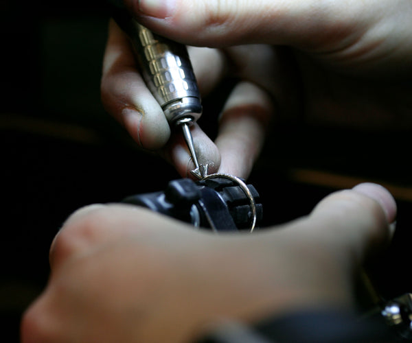 Guldsmed som tillverkare en diamantring och infattar diamanter med ett fattar verktyg. 