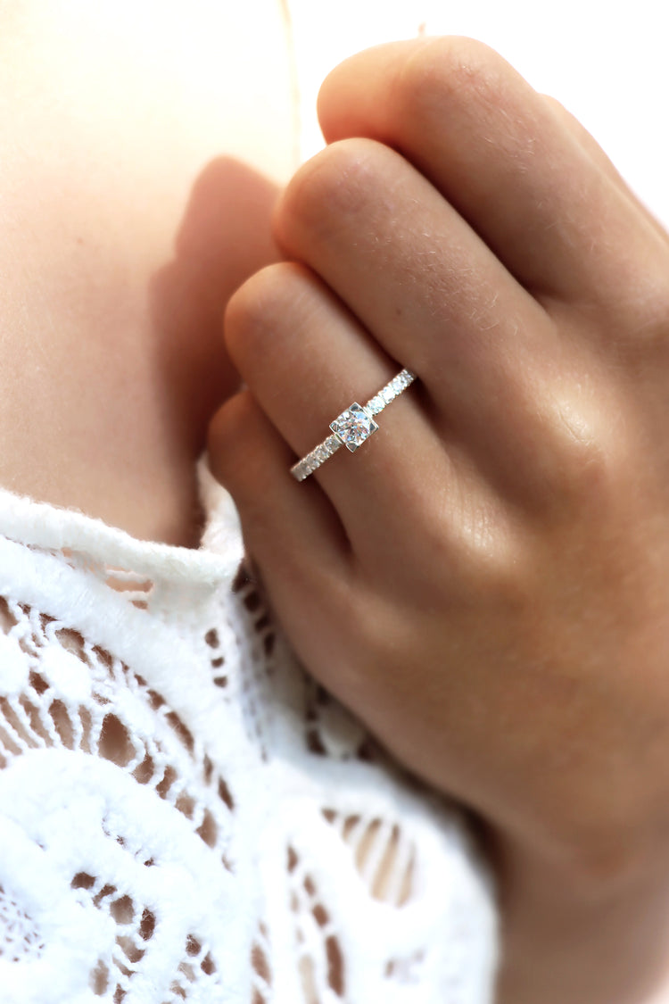 Tjej som bär en diamantring, modell solitärring med sidostenar som vigselring eller förlovningsring. Diamanten i mitten har fyrkantig fattning. 